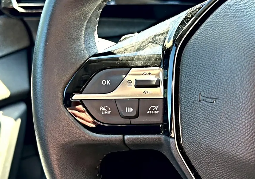 Gros plan sur les commandes gauche du volant cuir noir du Peugeot 408 Hybrid 145 allure 2025, boutons multifonctions visibles.