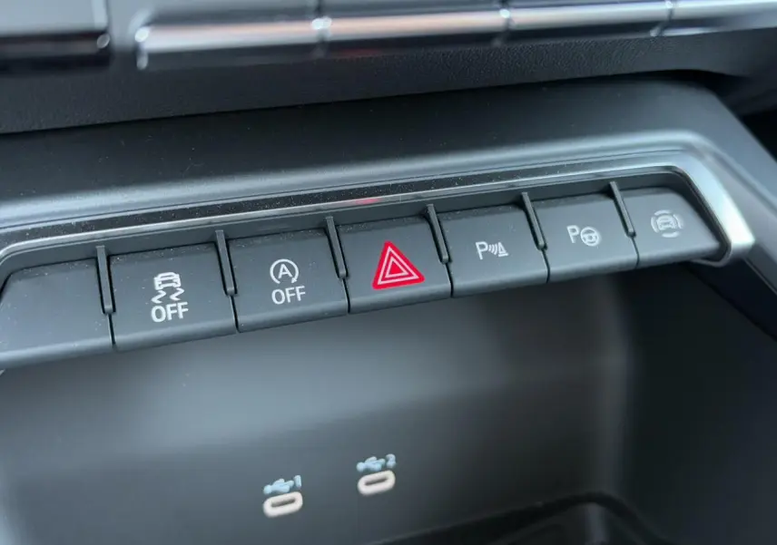 Gros plan sur les boutons de commande du tableau de bord de l'Audi A3 Sportback 2024 blanc Arkona, avec alertes et assistances.