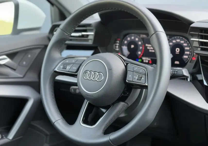 Volant cuir 3 branches multifonctions de l'Audi A3 Sportback 2024 vu de face côté conducteur, avec tableau de bord numérique.