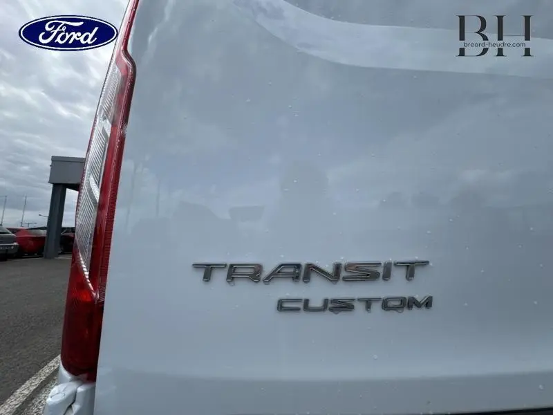 Gros plan sur l'arrière blanc glacier du Ford Transit Custom avec les badges "TRANSIT CUSTOM" visibles à gauche.