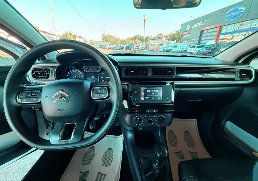 Vue intérieure du tableau de bord et volant noir d'une Citroën C3 blanche, avec écran tactile central et commandes manuelles.