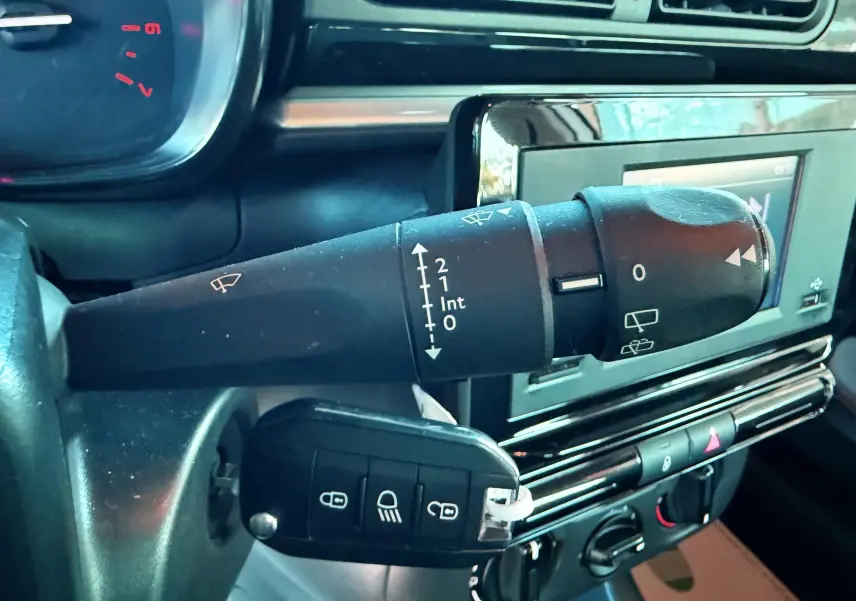 Gros plan sur la commande d'essuie-glace et la clé insérée dans le contacteur d'une Citroën C3 blanche, tableau de bord en arrière-plan.