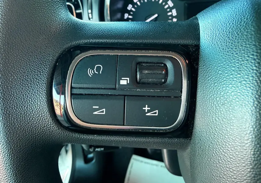 Gros plan sur les commandes du volant d'une Citroën C3 2021, boutons de volume et reconnaissance vocale visibles.