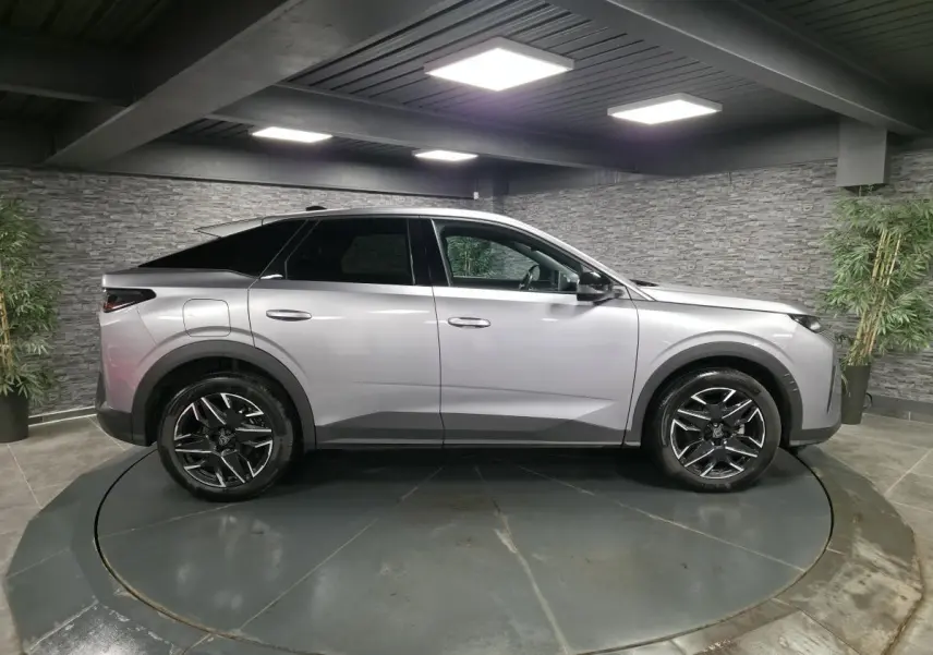 Vue latérale droite d’un Peugeot 3008 gris métallisé 2025 avec jantes alliage noires et toit noir en intérieur showroom.