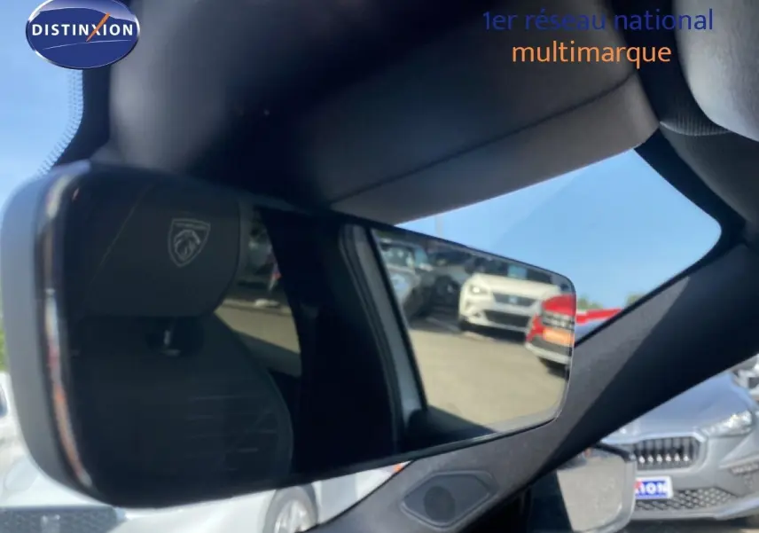 Rétroviseur intérieur avec logo Peugeot, reflétant le parking extérieur sous un ciel bleu.