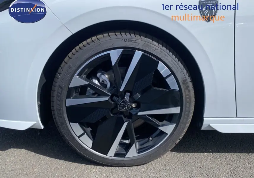 Gros plan sur la roue avant droite d'une Peugeot 308 Hybrid blanche, avec jante alliage noire et argentée au design moderne.