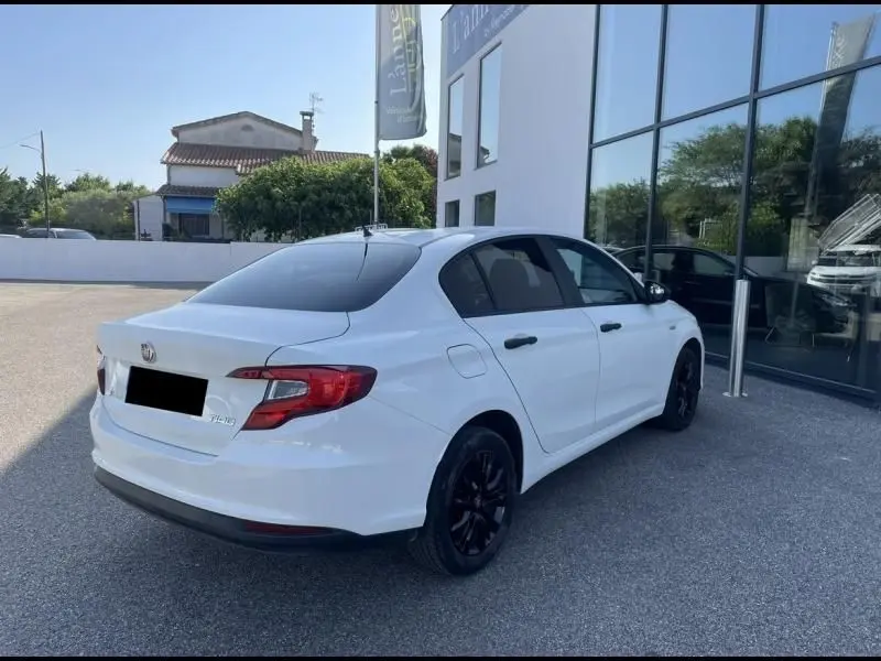 Vue 3/4 arrière droite d'une FIAT TIPO blanche 2019 avec jantes noires, garée devant un bâtiment vitré.