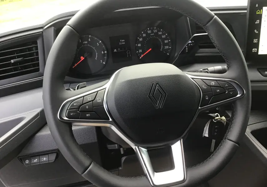Vue rapprochée du volant noir du Renault Master 2025 avec commandes intégrées et tableau de bord digital en arrière-plan.