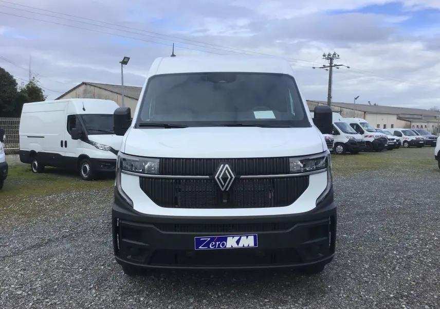 Vue avant d'un Renault Master blanc 2025 avec calandre noire et plaque "Zéro KM" sur un parking extérieur.