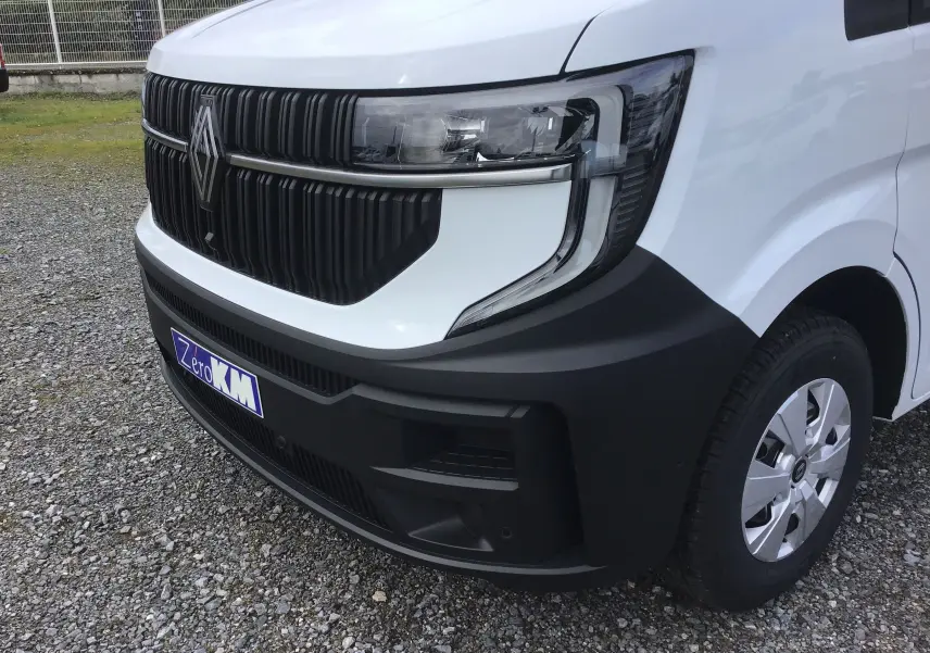 Vue avant droite du Renault Master blanc 2025 avec calandre noire et pare-chocs noir mat, sur sol gravillonné.