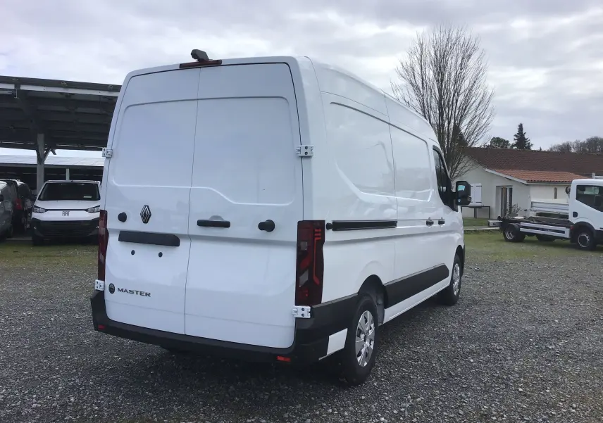 Renault Master blanc vu en 3/4 arrière droit, fourgon utilitaire avec feux arrière verticaux et protections noires.