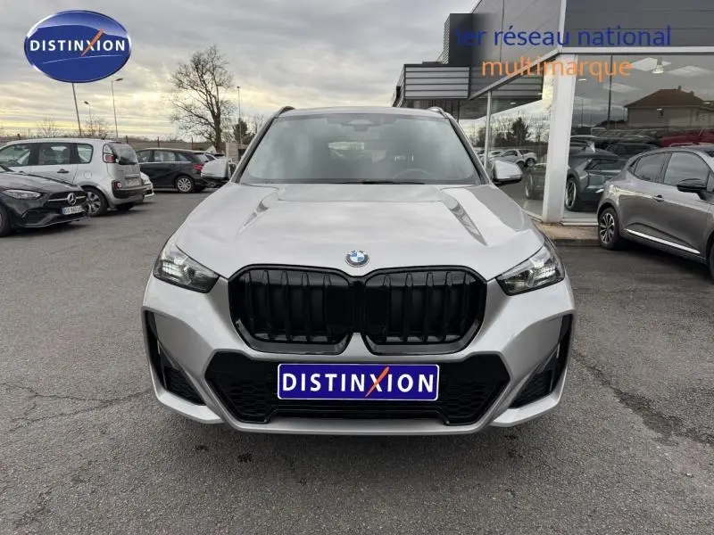 Vue de face d’un BMW X1 xDrive20d 2025 en Spacesilber métal avec calandre noire et phares LED allumés.