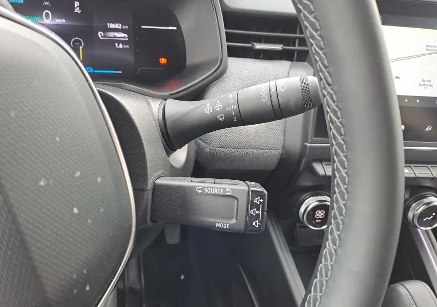 Vue rapprochée du volant et des commandes de la Renault Clio V 1.6 E-TECH hybride, intérieur noir avec tableau de bord digital.