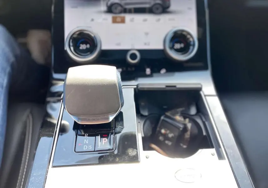 Gros plan sur la console centrale du Range Rover Velar gris, avec levier de boîte auto et écran tactile en arrière-plan.