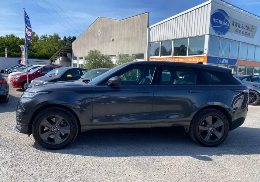 Profil côté gauche d'un Range Rover Velar gris tempête avec jantes satinées 19 pouces, stationné en extérieur.