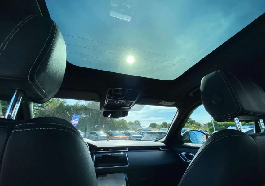 Vue intérieure avant du Range Rover Velar gris Tempête avec toit panoramique et sièges noirs en cuir.