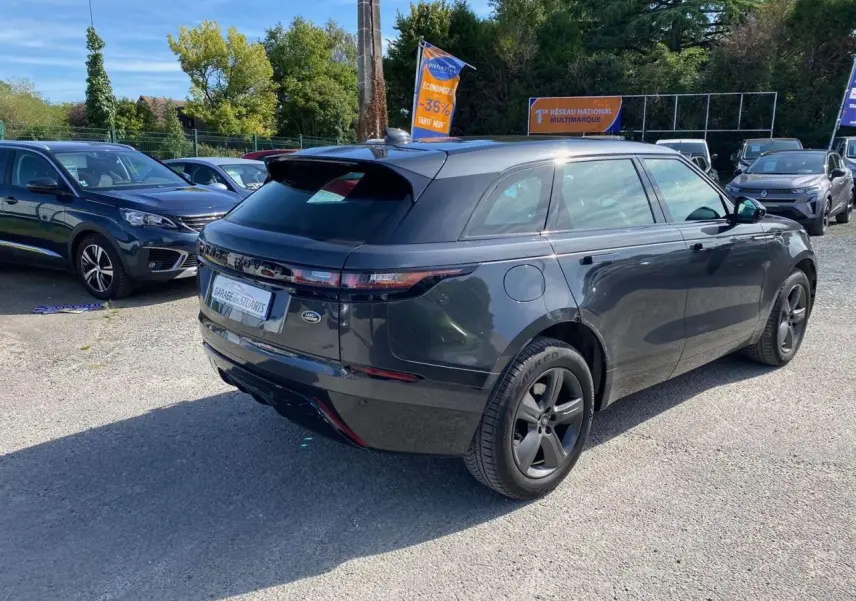 Vue 3/4 arrière droite du Range Rover Velar gris Tempête avec jantes satinées et toit panoramique visible en extérieur.