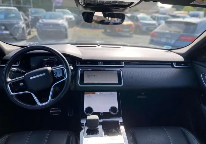 Intérieur du Range Rover Velar 2022 vu de face, tableau de bord noir avec écran tactile et volant multifonction.