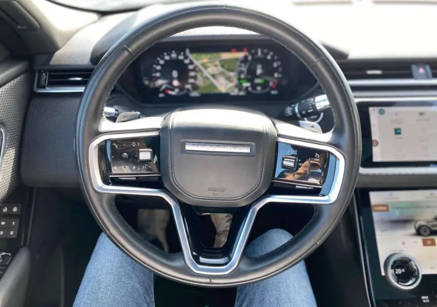 Vue rapprochée du volant cuir noir du Range Rover Velar 2022, avec tableau de bord numérique et écran tactile central.