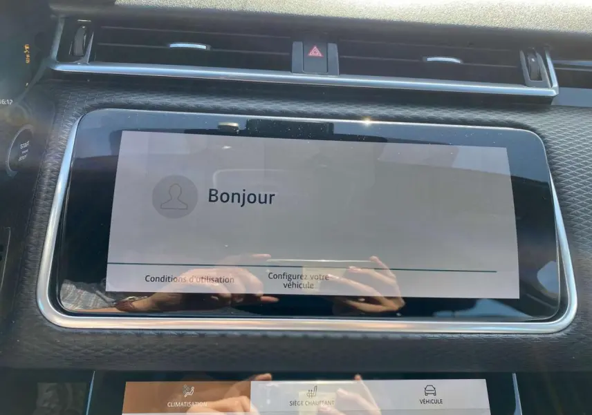 Écran tactile central affichant un message de bienvenue dans l'habitacle du Range Rover Velar gris Tempête, vue de face rapprochée.