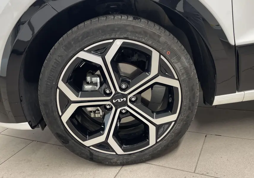 Gros plan sur la roue avant gauche d’un KIA NIRO blanc 2025, mettant en valeur la jante noire et argentée au design moderne.