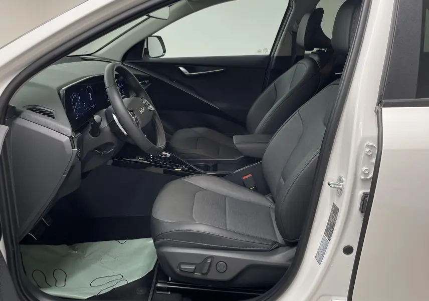 Intérieur côté conducteur du Kia Niro blanc 2025, sièges noirs et tableau de bord digital moderne visible.