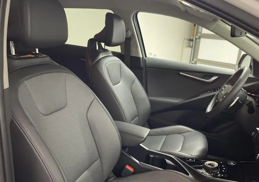 Vue intérieure côté conducteur du Kia Niro 2025 blanc, sièges en cuir noir et tableau de bord moderne.