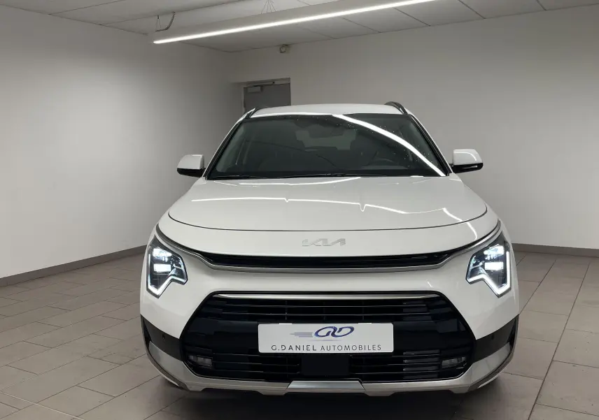 Vue frontale d’un KIA NIRO blanc 2025 hybride avec phares LED en forme de flèche et calandre noire distinctive.