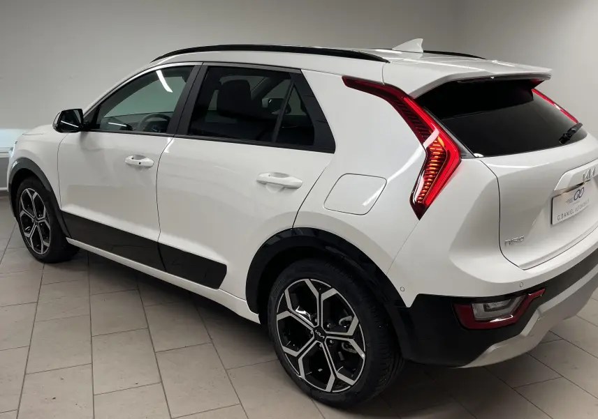 KIA NIRO blanc vue 3/4 arrière côté gauche, avec feux arrière LED en forme de boomerang et jantes noires stylisées.
