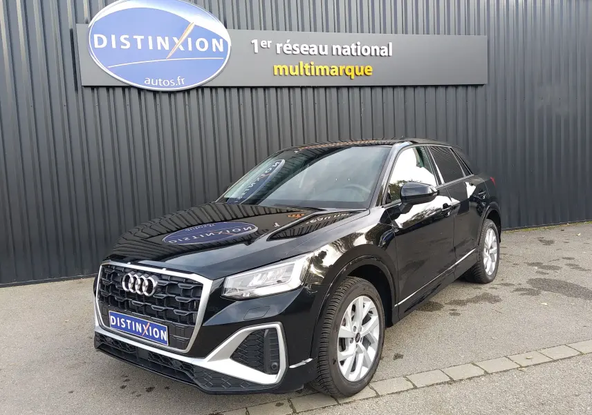 Audi Q2 35 TFSI S-Line noir mito metal en 3/4 avant droit, stationné devant un mur gris avec enseigne Distinxion.