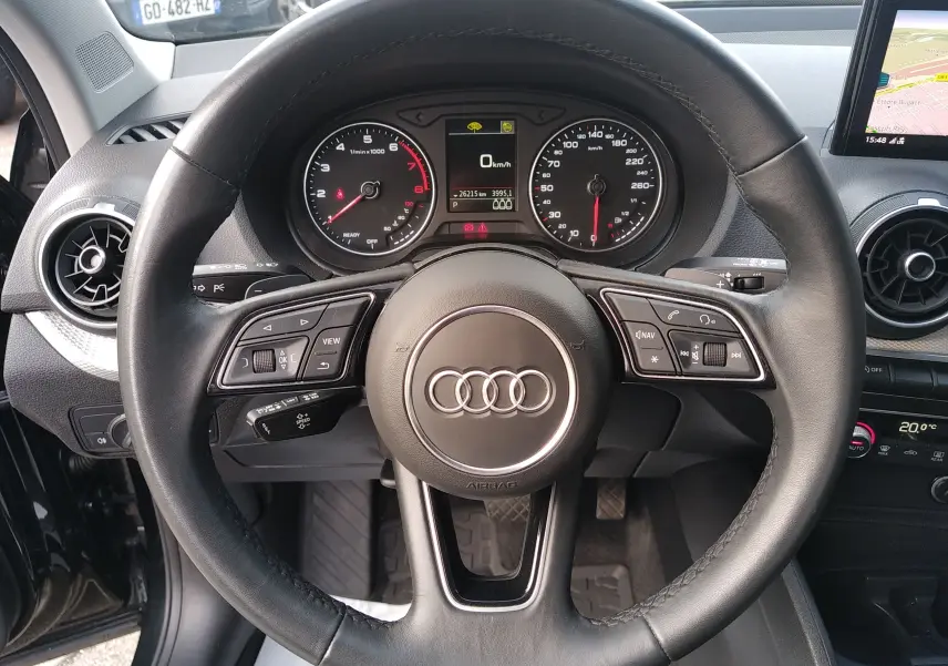 Vue rapprochée du volant en cuir noir de l'Audi Q2 35 TFSI S-Line 2023 avec tableau de bord et écran GPS visible.
