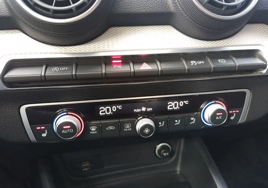 Vue rapprochée de la console centrale noire de l'Audi Q2 35 TFSI 2023, montrant les commandes de climatisation digitale et boutons fonctionnels.