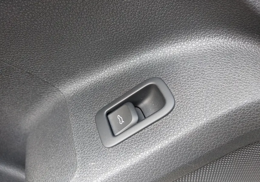 Bouton d'ouverture électrique du hayon sur le revêtement intérieur noir du coffre de l'Audi Q2 35 TFSI S-Line 2023.