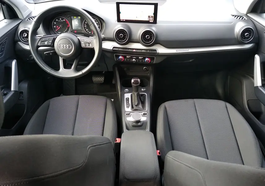 Vue intérieure avant de l'Audi Q2 35 TFSI S-Line 2023, tableau de bord noir avec écran central et sièges tissu gris.