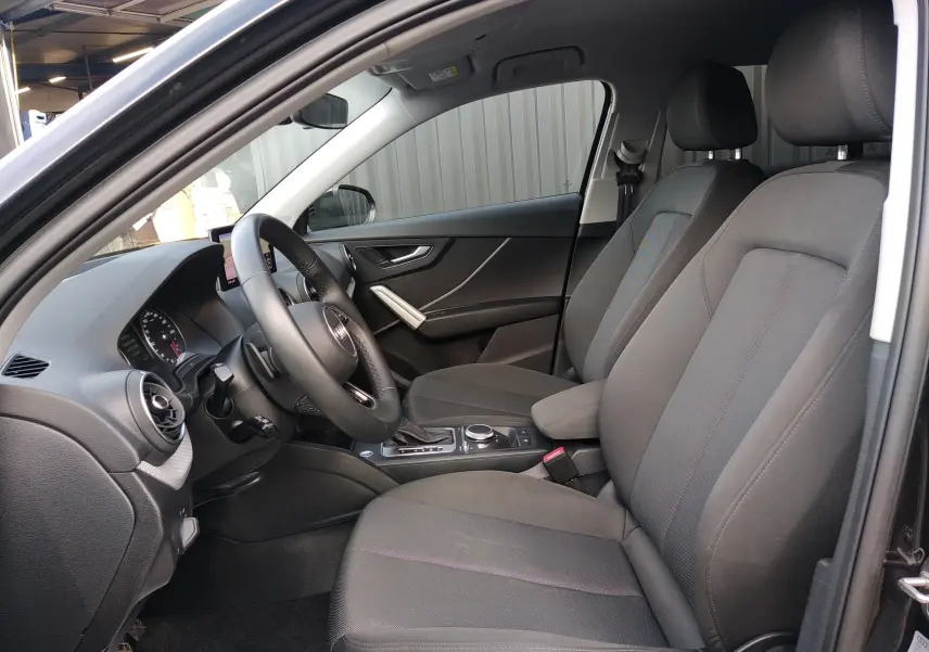 Vue intérieure côté conducteur de l'Audi Q2 35 TFSI S-Line 2023 avec sièges tissu gris et tableau de bord noir.