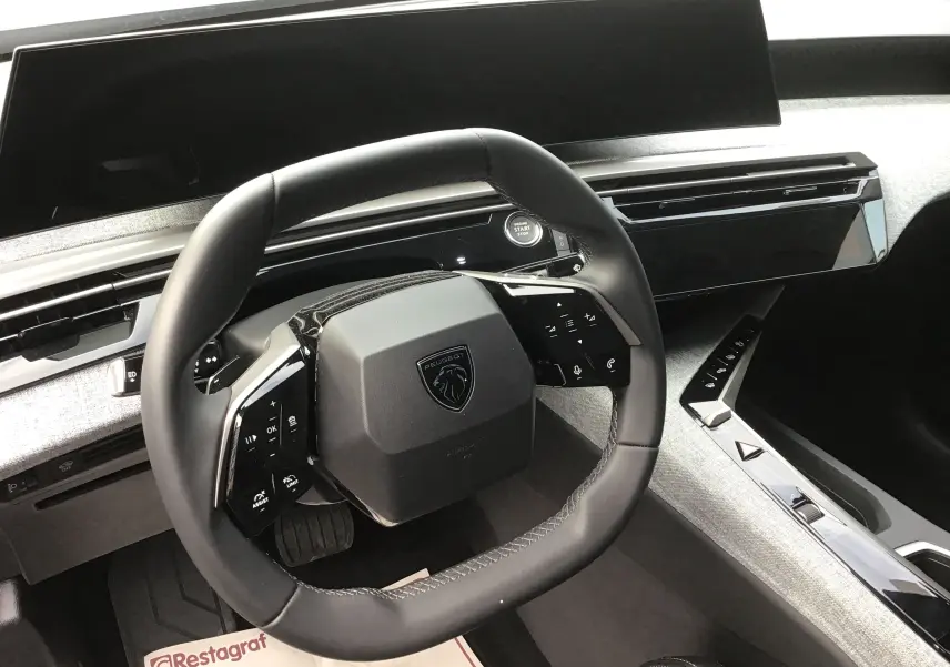 Vue intérieure centrée sur le volant carré du Peugeot 3008 2026, avec tableau de bord numérique et finition gris clair.
