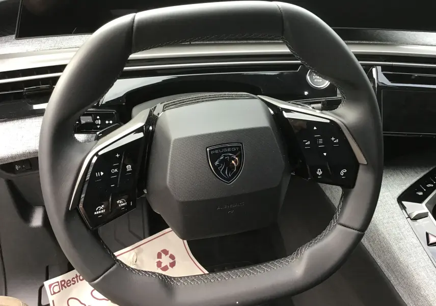 Vue rapprochée du volant cuir noir du Peugeot 3008 1.2 Hybrid 145 Allure avec commandes intégrées et tableau de bord gris.