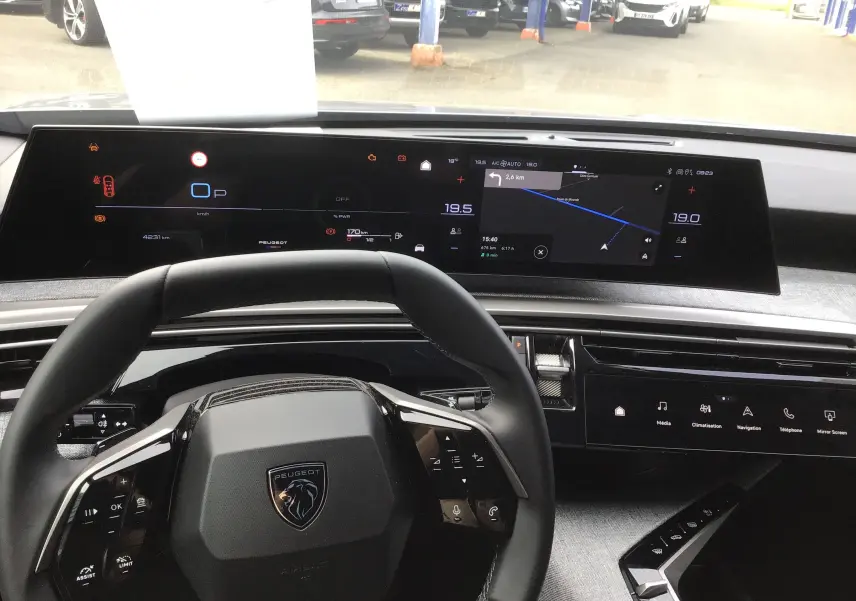 Vue intérieure centrée sur le volant et le tableau de bord numérique du Peugeot 3008 1.2 Hybrid 145 gris Artense, avec écran tactile et navigation.