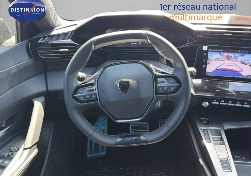 Vue intérieure centrée sur le volant noir cuir GT de la Peugeot 308 Hybrid 145ch, avec écran tactile et caméra de recul visible.
