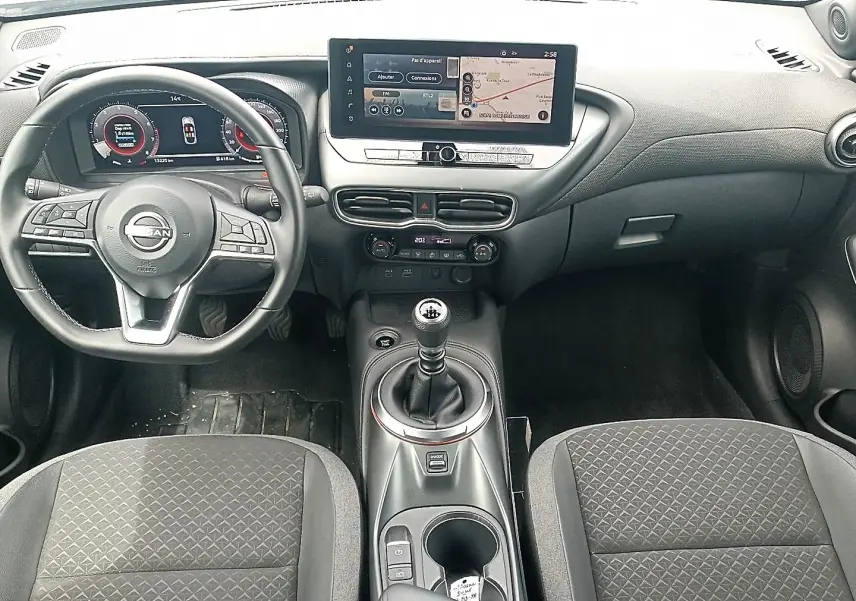 Vue intérieure avant du Nissan Juke 2025, tableau de bord et volant multifonction avec levier de vitesse manuel.