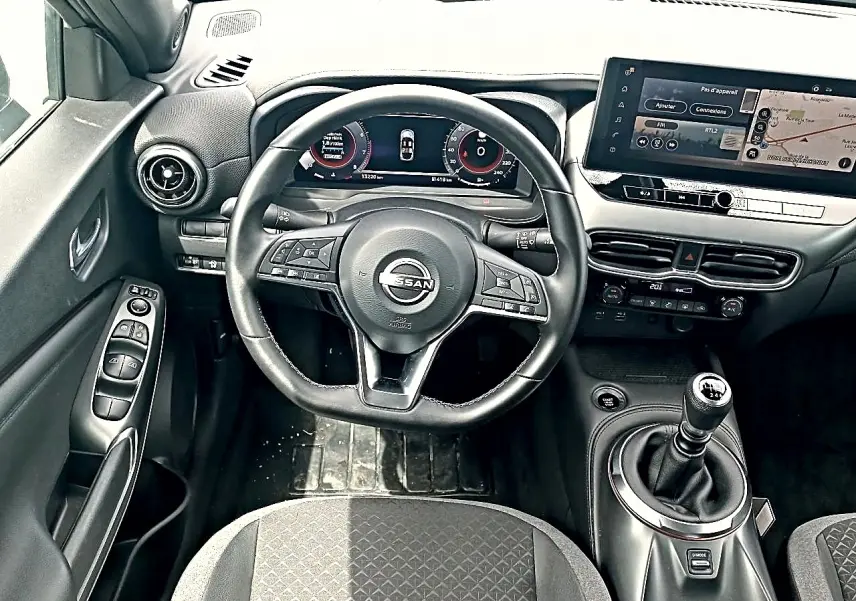 Vue intérieure frontale du poste de conduite noir du Nissan Juke 2025 avec volant cuir multifonction et boîte manuelle.