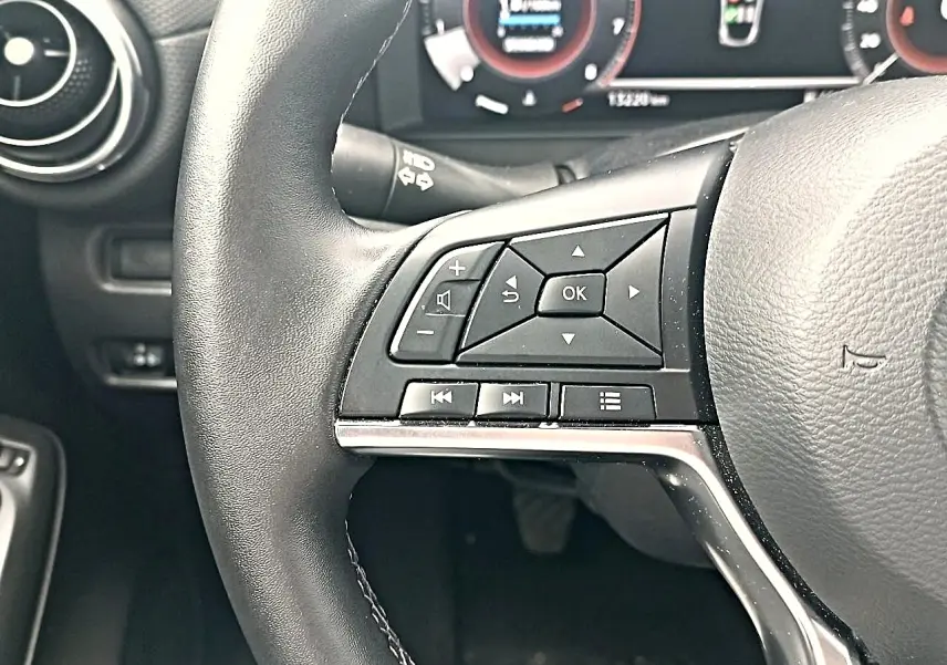 Gros plan sur le volant cuir noir multifonction côté gauche du Nissan Juke gris, avec commandes audio et navigation.