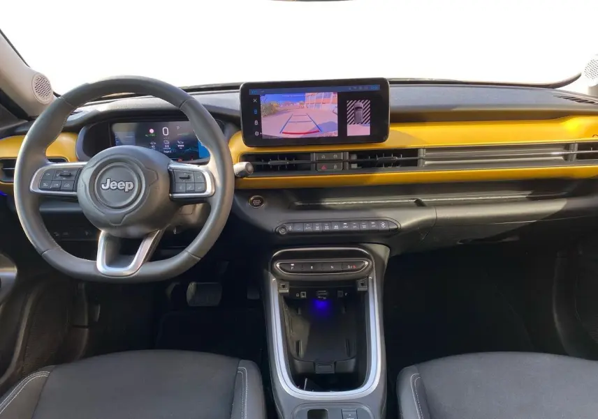 Intérieur du Jeep Avenger électrique 2023 vu de face, tableau de bord noir avec bande jaune et écran tactile central.