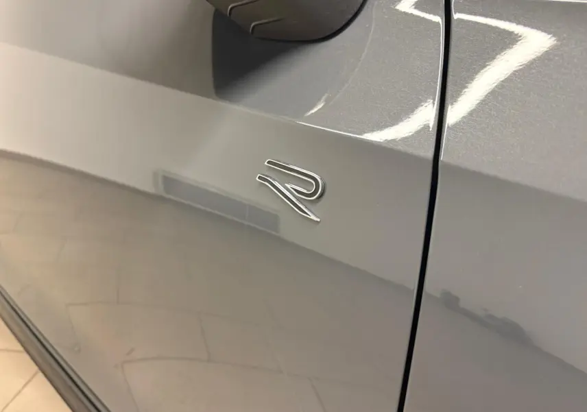 Gros plan sur l'emblème R sur la porte côté gauche d'une Volkswagen Golf gris dauphin brillante.