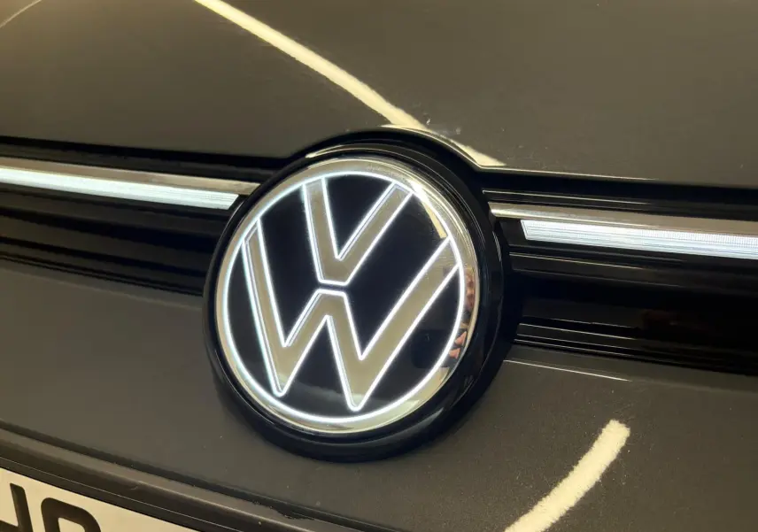 Gros plan sur le logo Volkswagen éclairé sur la calandre d'une Golf 1.5 eTSI gris dauphin, vue avant.