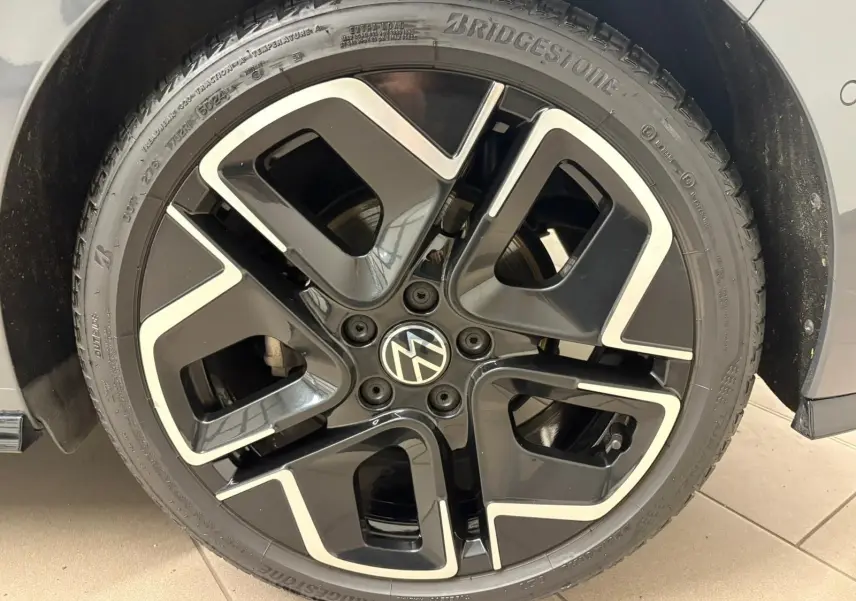 Gros plan sur la jante noire et argentée d'une Volkswagen Golf Gris Dauphin, mettant en valeur le logo VW central.