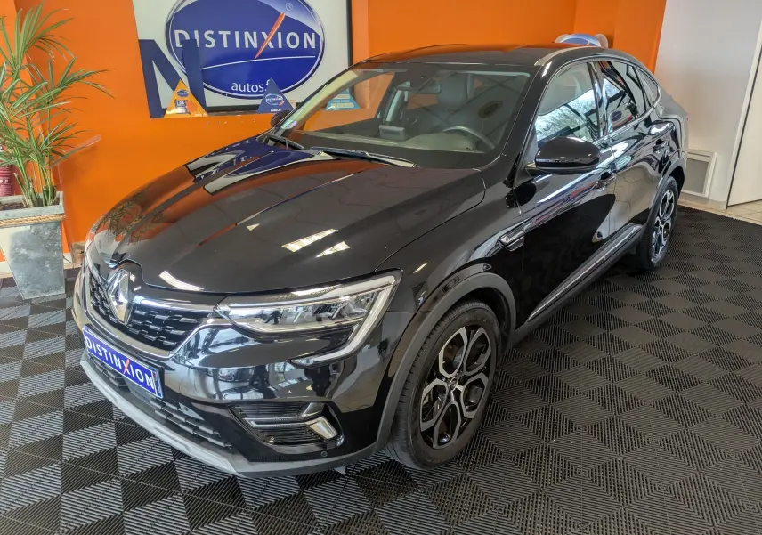 Renault Arkana noir en 3/4 avant droit, avec jantes bi-ton et calandre chromée dans un showroom orange.