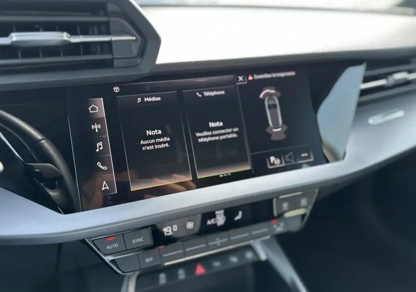 Vue rapprochée de la console centrale de l'Audi A3 Sportback 2024 blanche, affichant l'écran tactile multimédia et les commandes climatiques.