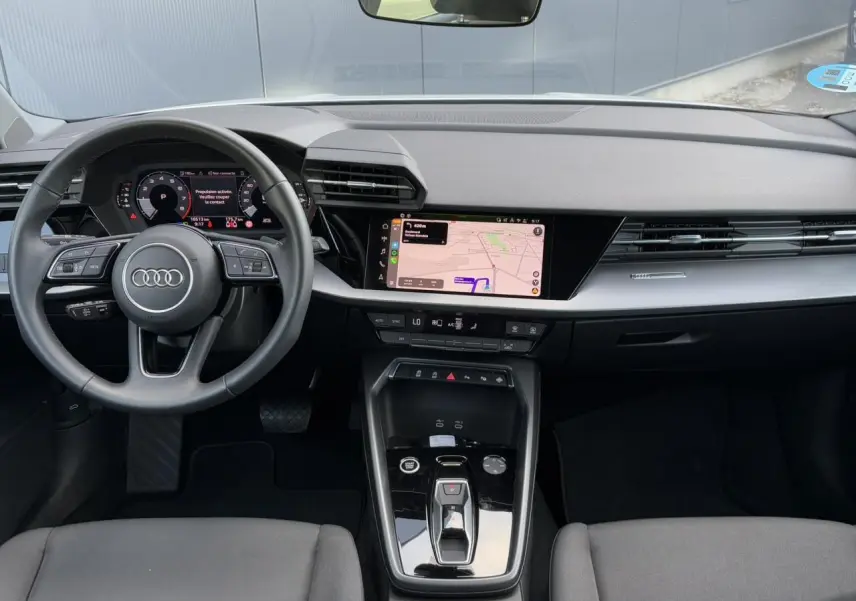 Vue intérieure frontale de l'Audi A3 Sportback 2024, tableau de bord moderne avec écran tactile et volant cuir multifonctions.