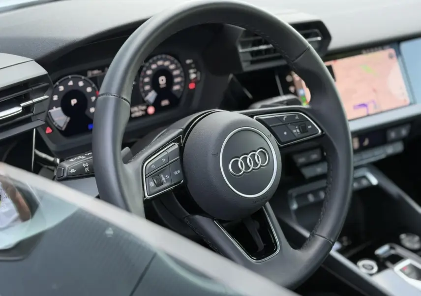 Volant cuir trois branches de l'Audi A3 Sportback 2024 vu côté conducteur avec tableau de bord numérique et écran tactile.